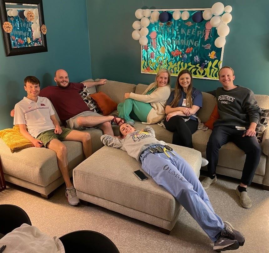 group picture of six pediatric residents lounging on couch and ottoman at indoor event